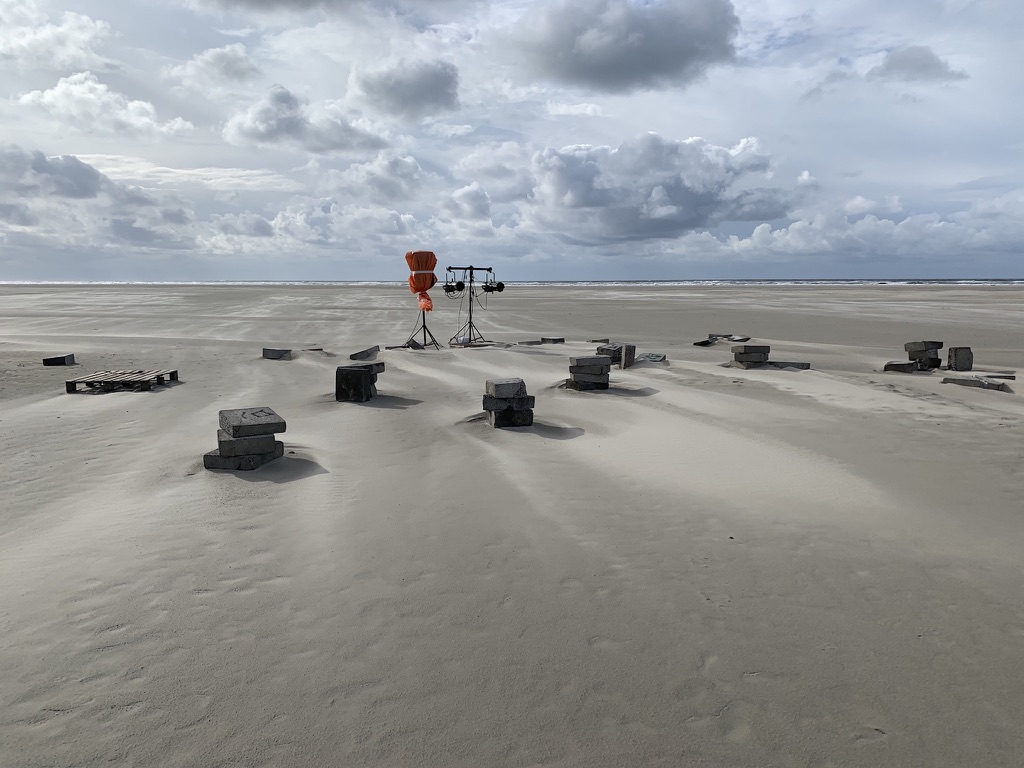 Outdoors, daytime. A vast beach and a vast sky with clouds drifting across it. There are no people. The preset performance area shows how the wind affects the movement of sand around the blocks overnight.